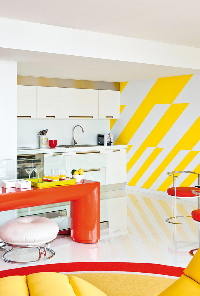 Composição em vermelho, amarelo e branco para esta cozinha integrada à sala de estar