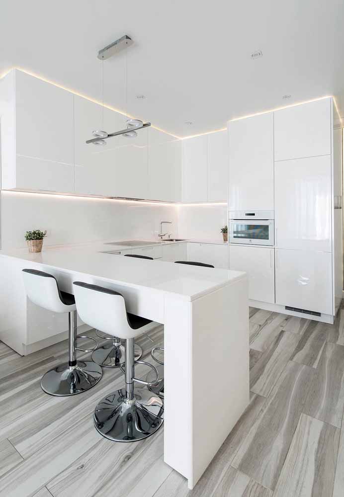 Cozinha branca pequena ao estilo americano, bancada com quatro cadeiras com detalhe de pés em inox para realçar o piso imitando madeira