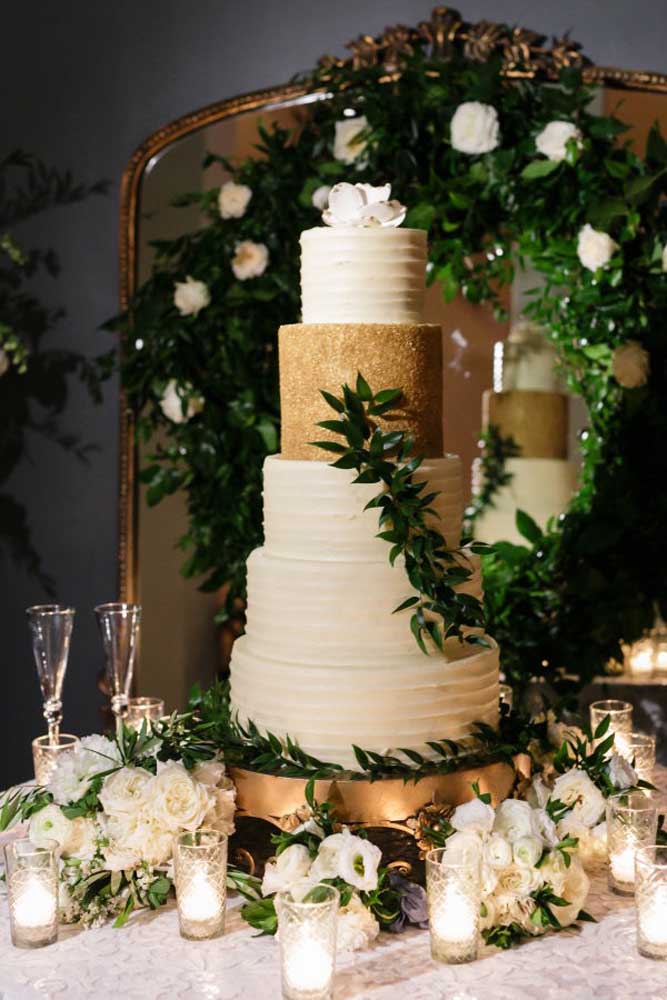 As flores chamadas de copo de leite são as mais usadas na decoração de casamento. Nesse caso, o arranjo de flores foi colocado na mesa do bolo junto com alguns copos com velas.