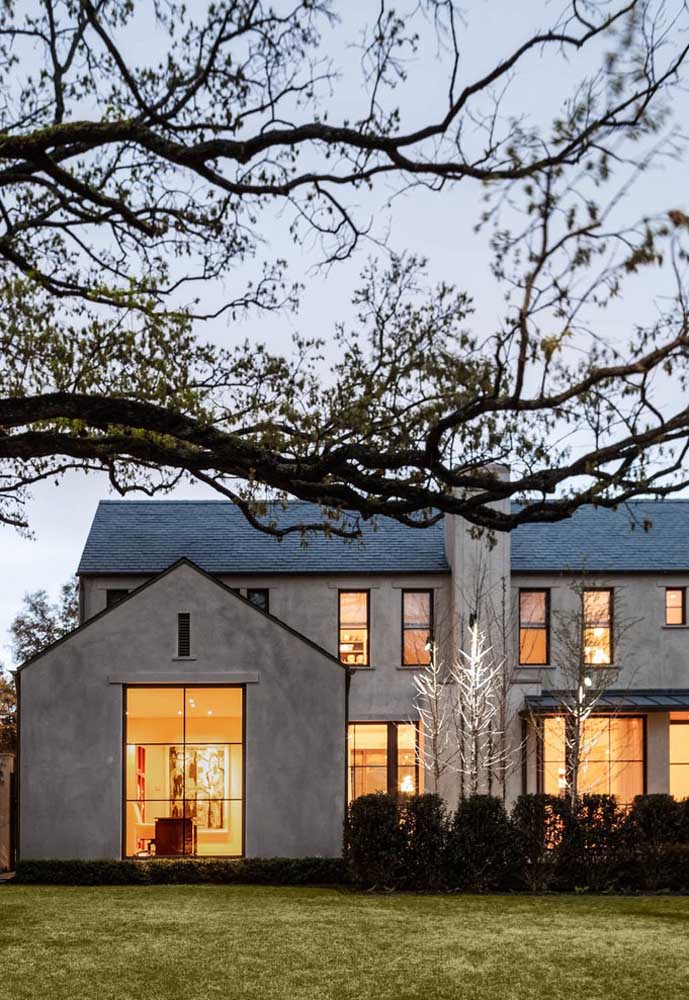 Casa ampla, espaçosa com destaque para as grandes janelas de vidro e revestimento de cimento queimado; o jardim na frente completa a fachada