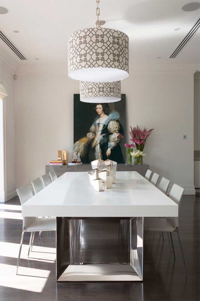Sala de jantar de casa grande: janelas amplas, mesa grande, quadro gigante na parede e luminárias suspensas; repare que o segredo da decoração de ambientes amplos é a proporção