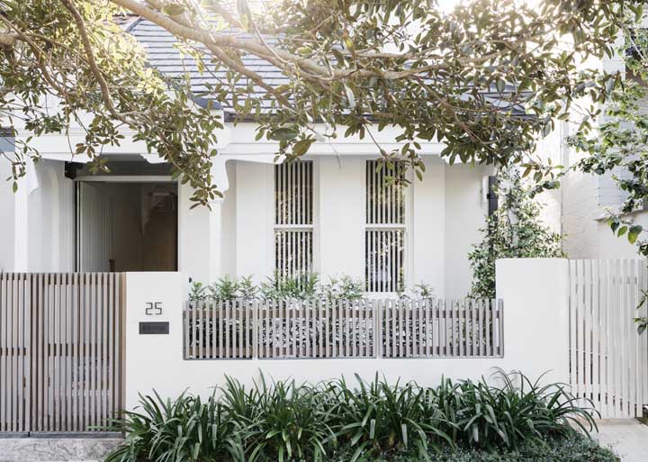 De muro baixo e paredes brancas, essa casa simples traz um belo jardim na entrada