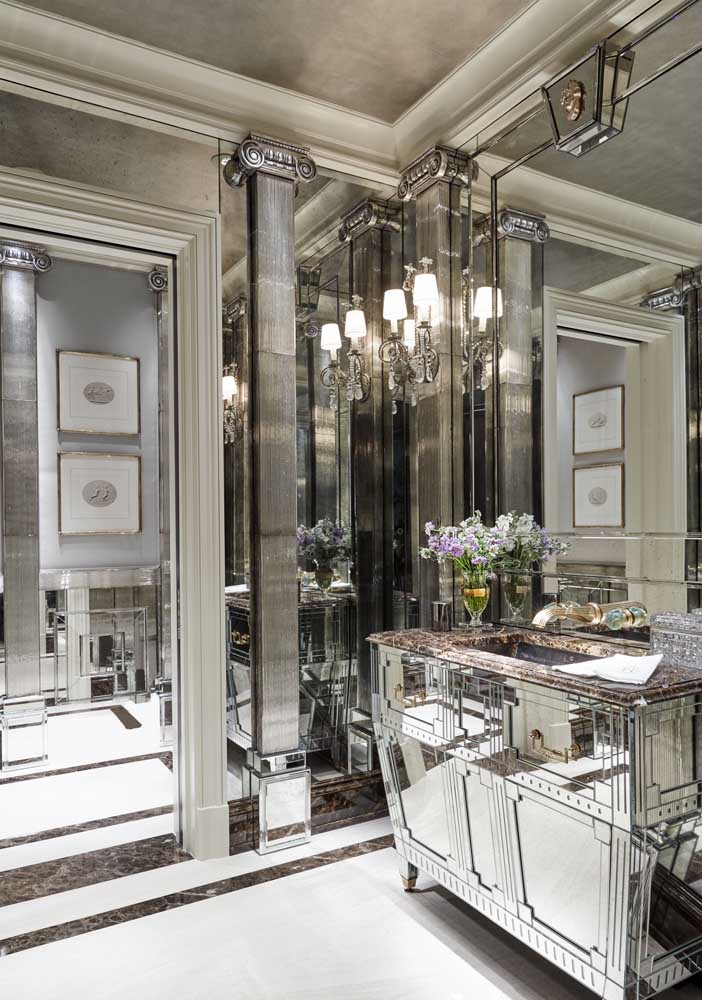 Banheiro de decoração clássica com móveis espelhados e espelho bisotado forrando as paredes 