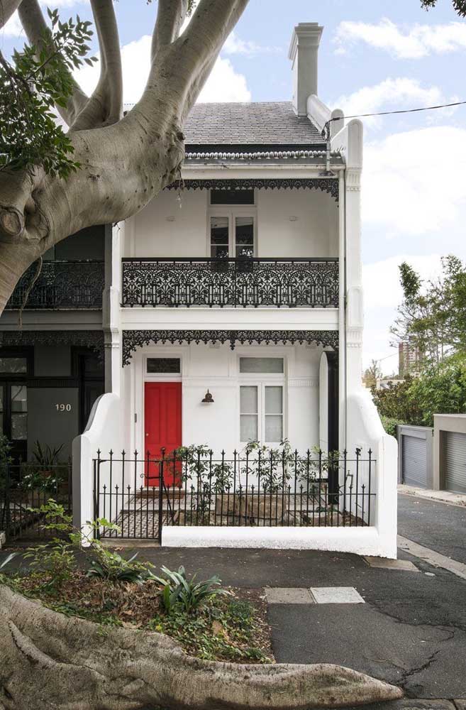 Fachada simples, de casa em estilo clássico; o grande destaque vai para a porta pintada de vermelho e para as grades de ferro lindamente desenhadas 