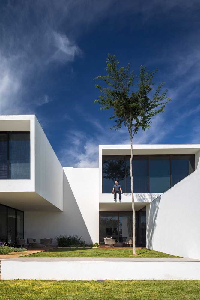 Fachada de casa moderna, branca, com grandes aberturas de vidro e um jardim de grama