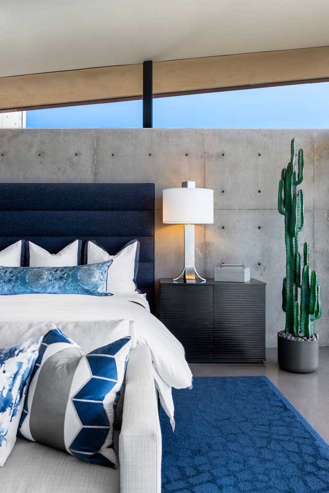 No quarto do casal, a elegância do azul marinho forma um lindo contraste com a rusticidade do cimento queimado