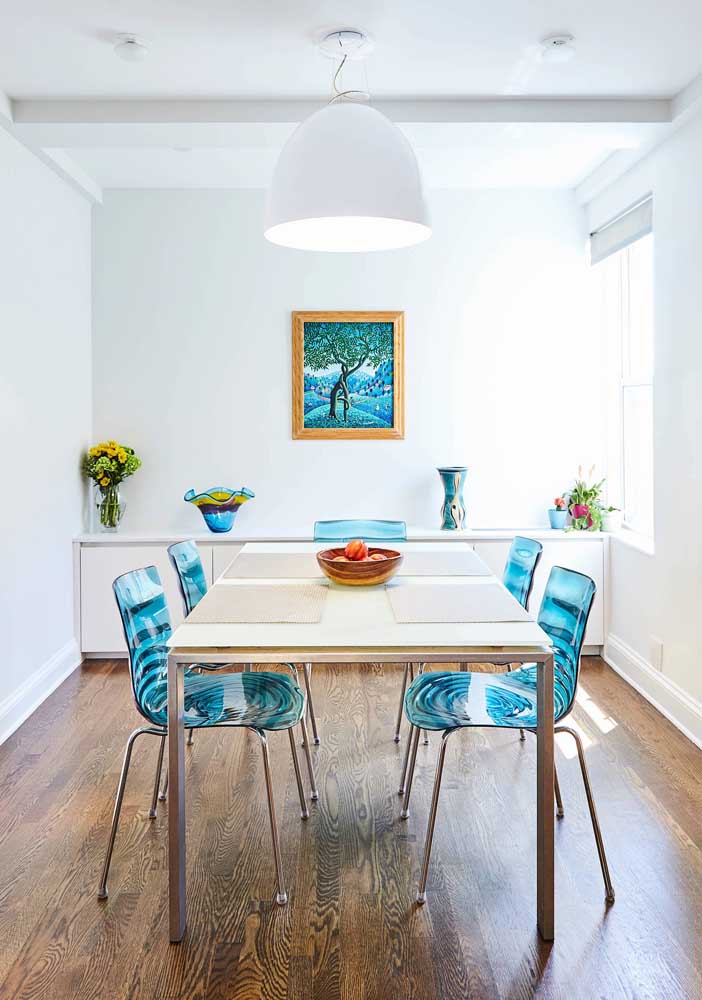 Essa sala de jantar clean trouxe cadeiras de acrílico azul para combinar com os detalhes da decor