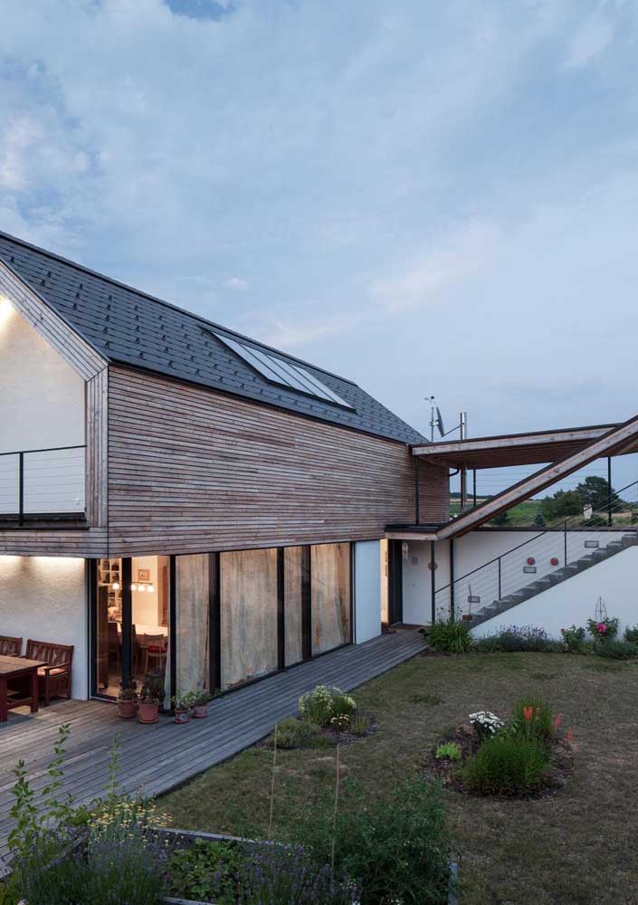 Casa em L simples com varanda e fachada em madeira; destaque para o terraço ao fundo da casa