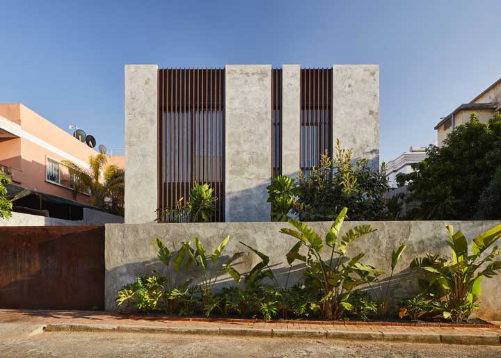 Casa planejada em estilo moderno com fachada de cimento queimado e muro cercado por plantas 