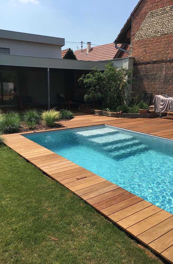 As plantas e o deck de madeira deixam o espaço ao redor da piscina mais convidativo e acolhedor