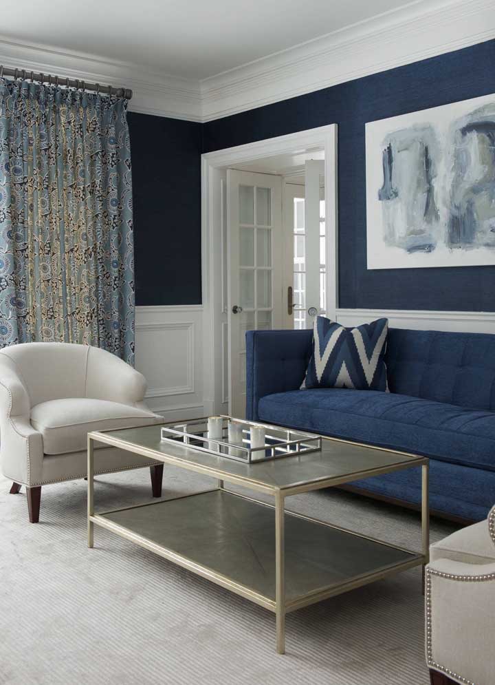 Parede e sofá compartilham o mesmo tom de azul nessa sala de estilo clássico e sóbrio
