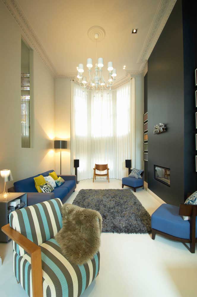 A sala de pé direito alto trouxe um sofá azul acompanhado de duas poltronas na mesma cor