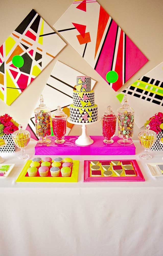 Sugestão de mesa de bolo para a festa neon; repare que os quadros aos fundos fazem a vez dos tradicionais painéis