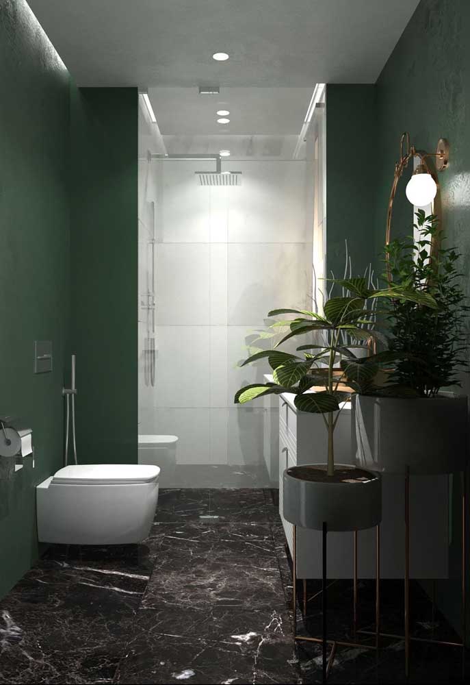 A parede verde traz profundidade ao banheiro decorado com plantas; o chão de mármore completa a proposta com elegância