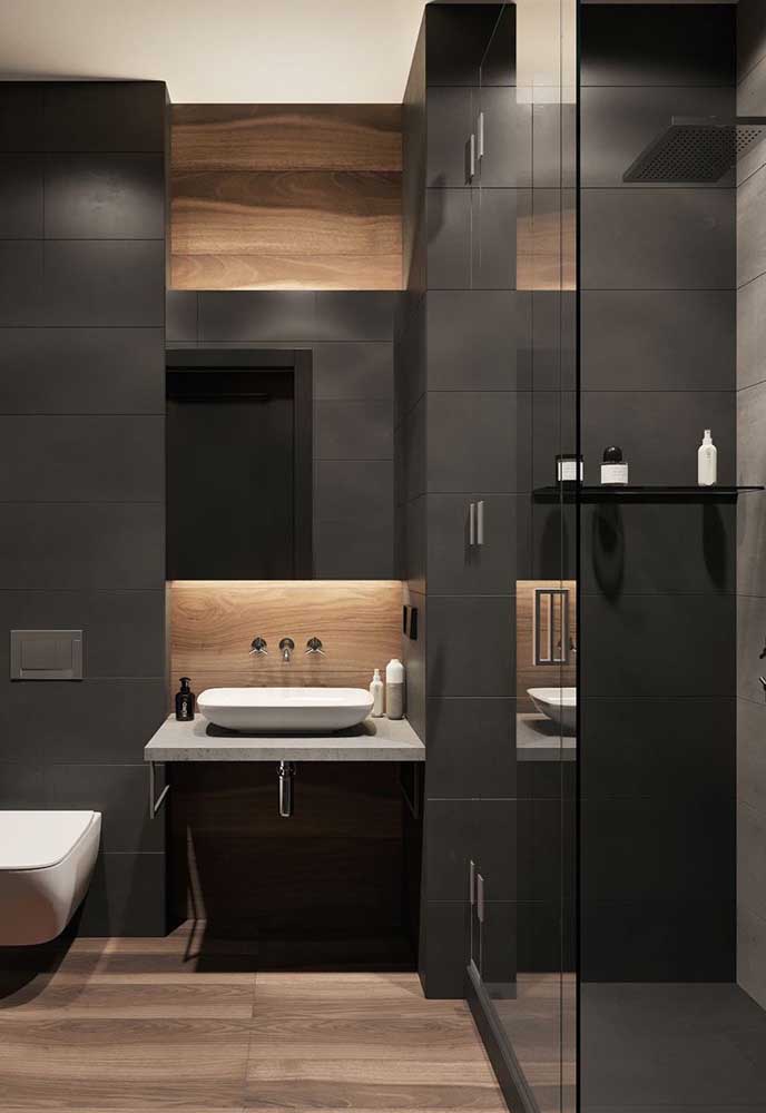 Como é o caso desse banheiro com parede escura, mas com piso de madeira para diferenciar o ambiente.