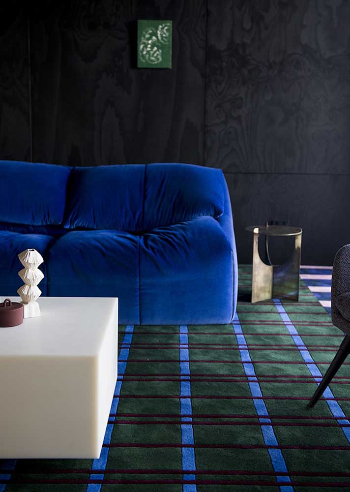 Sala colorida com sofá azul, parede preta e tapete verde