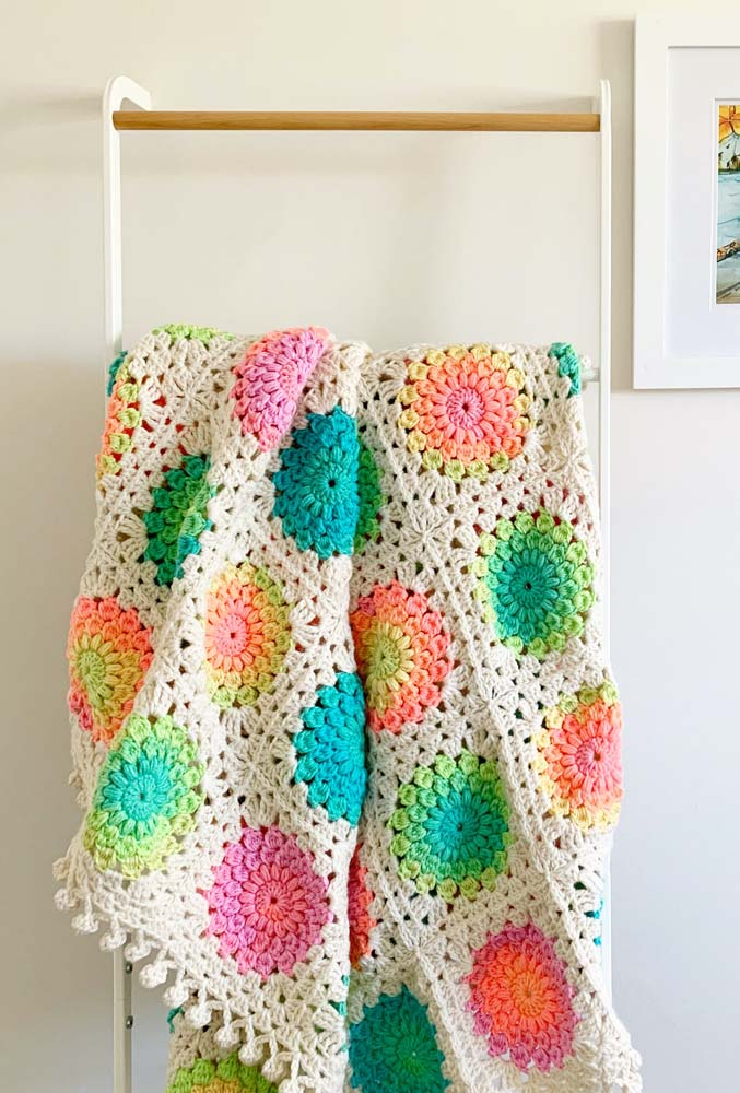 Para completar a decoração Cottage Core, um tapete de crochê com square colorido formando uma flor com linha mesclada no centro. 