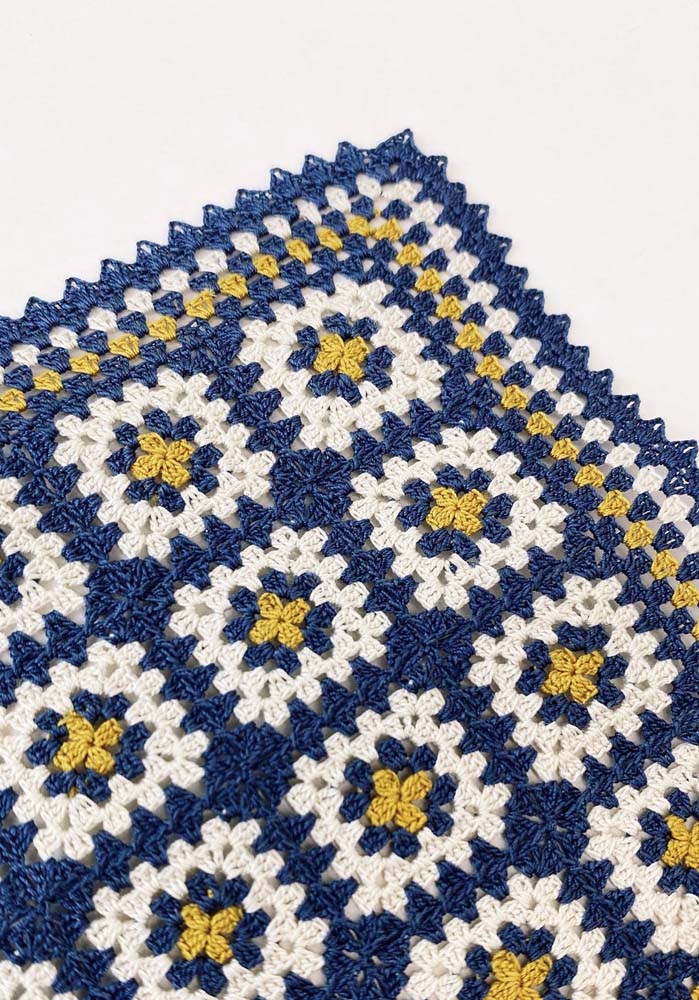 Tapete de crochê com square colorido em azul, branco e amarelo, com florzinhas no centro. 