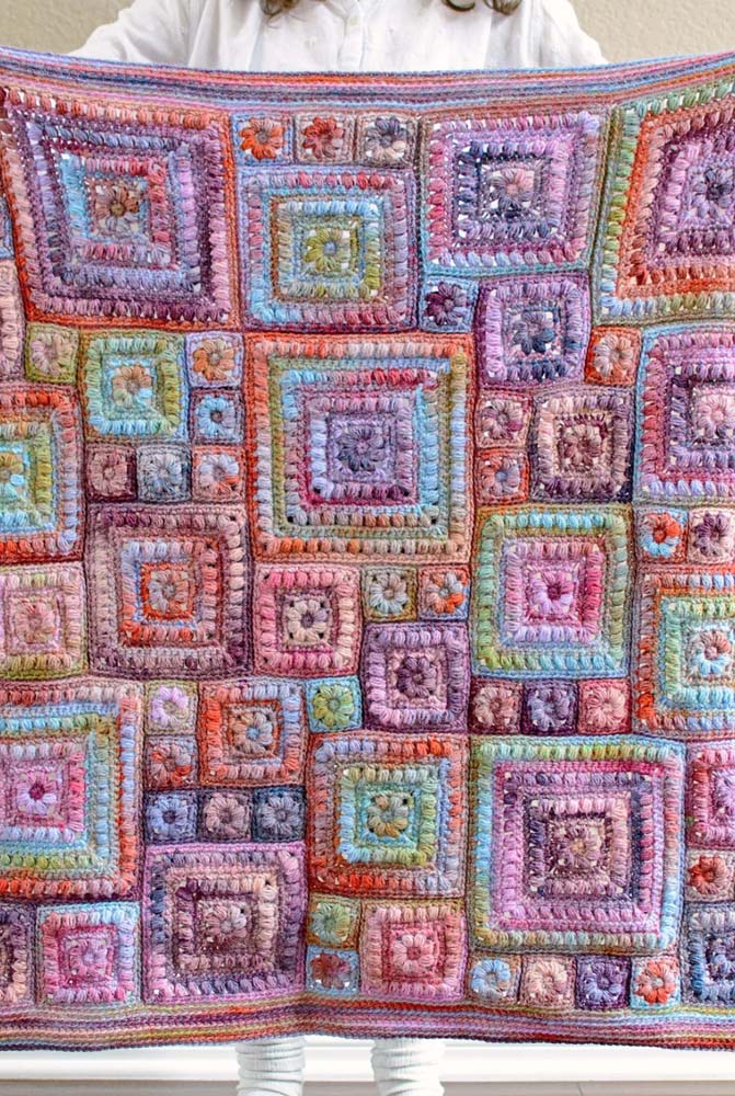 Um tapete de crochê cheio de textura, formado por squares quadrados de diferentes tamanhos, todos com o mesmo padrão e linha mesclada.