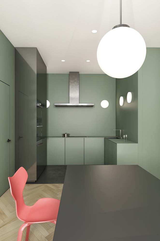 Cozinha integrada à sala de jantar numa decoração moderna com parede e bancadas em verde musgo claro, armário e mesa cinza chumbo e cadeira coral.