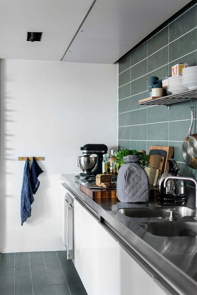 O revestimento verde musgo cinzento cobre todo o piso e sobe a parede da pia nesta cozinha simples e moderna. 