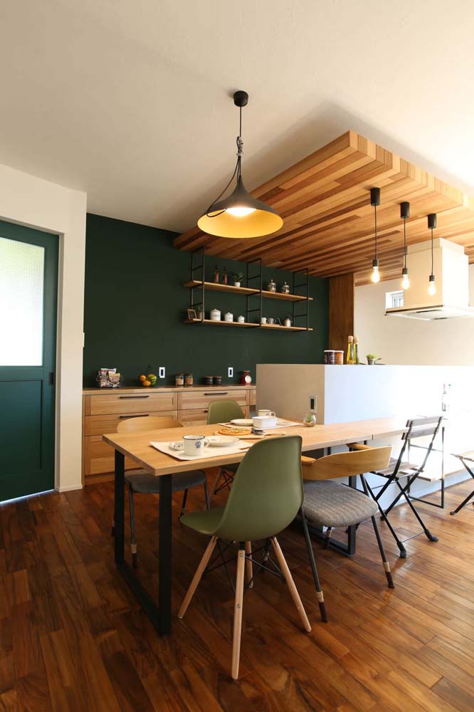 Combinação de diferentes tons de verde, com a parede num tom escuríssimo e um verde musgo claro em duas das cadeiras da mesa. 