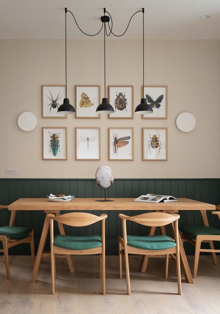 Nesta sala de jantar, se destacam a meia parede revestida com painel verde musgo escuro e os estofados das cadeiras de madeira clara. 