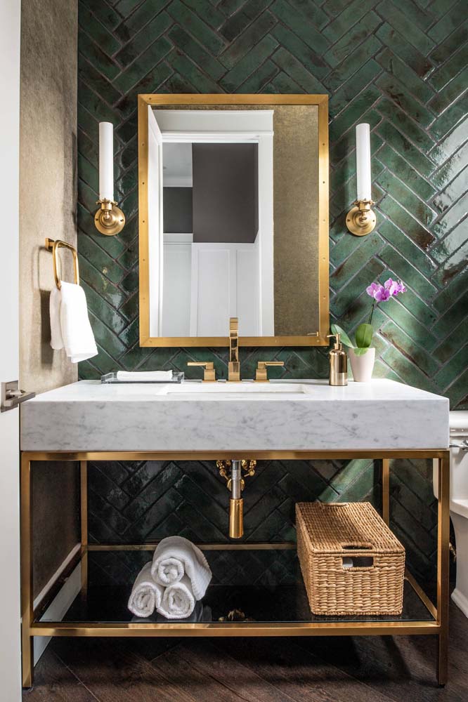 Os metais dourados contrastam com os azulejos verde musgo dispostos em padrão de escama de peixe e deixam este banheiro ainda mais elegante.