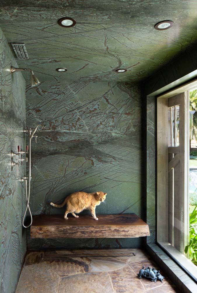 Já nesta ampla ducha, o verde musgo aparece em outro elemento natural: a pedra que reveste tanto as paredes como o teto do ambiente.