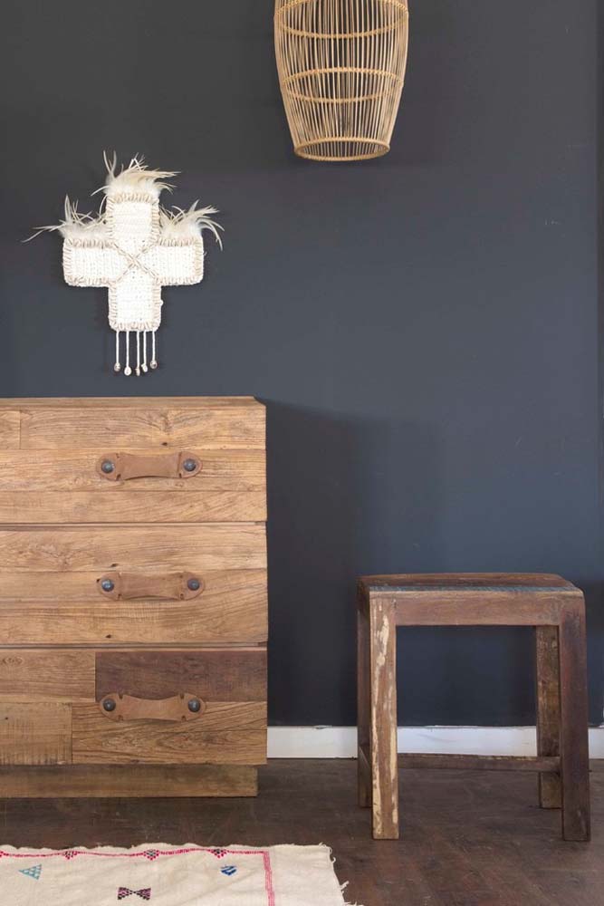 No espaço com parede preta, a cômoda, o banquinho e a luminária pendente de madeira se destacam e formam um conjunto.