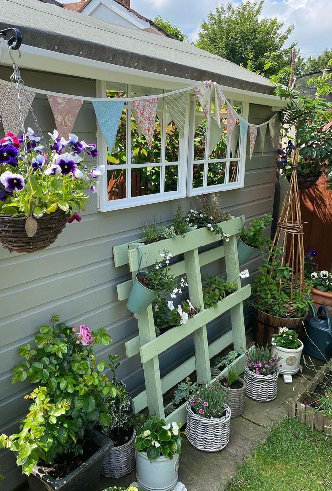 Um jardim super charmoso e com floreira de pallet encostada na parede, vasos pendentes e de chão para cultivar suas plantas e relaxar.