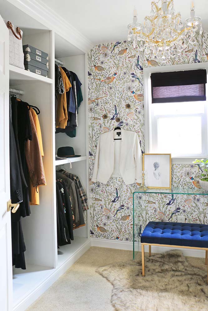 Closet com guarda roupa branco, papel de parede com ilustrações de pássaros e um lustre luxuoso. 