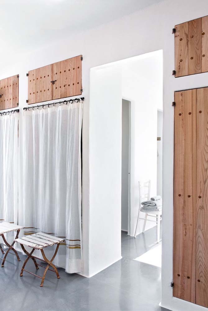 Num visual mais rústico, um guarda roupa de gesso com portas de madeira na parte de cima e, embaixo, uma cortina simples.