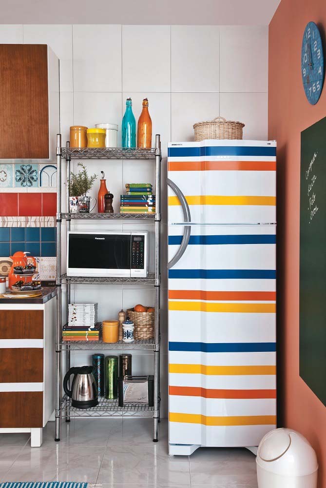 A geladeira não fica de fora dessa decoração de cozinha colorida e ganha listras adesivas em azul, amarelo e laranja sobre o branco.