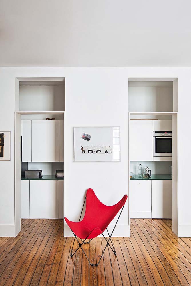Posicionada num cantinho entre uma porta e outra, a cadeira vermelha torna-se o centro das atenções nesse ambiente todo branco. 