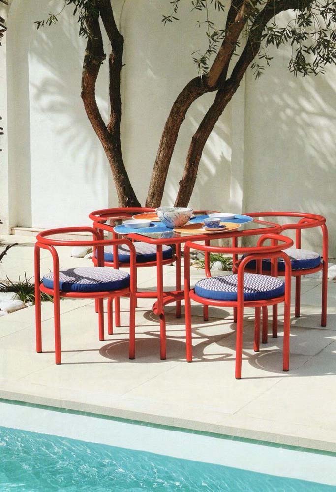 Já na área da piscina, as cadeiras vermelhas são certeiras para contrastar com o azul da água.