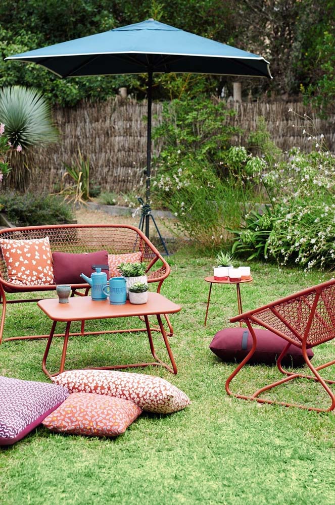 As almofadas também trazem mais conforto na o visual desse living ao ar livre com cadeiras vermelhas de metal.