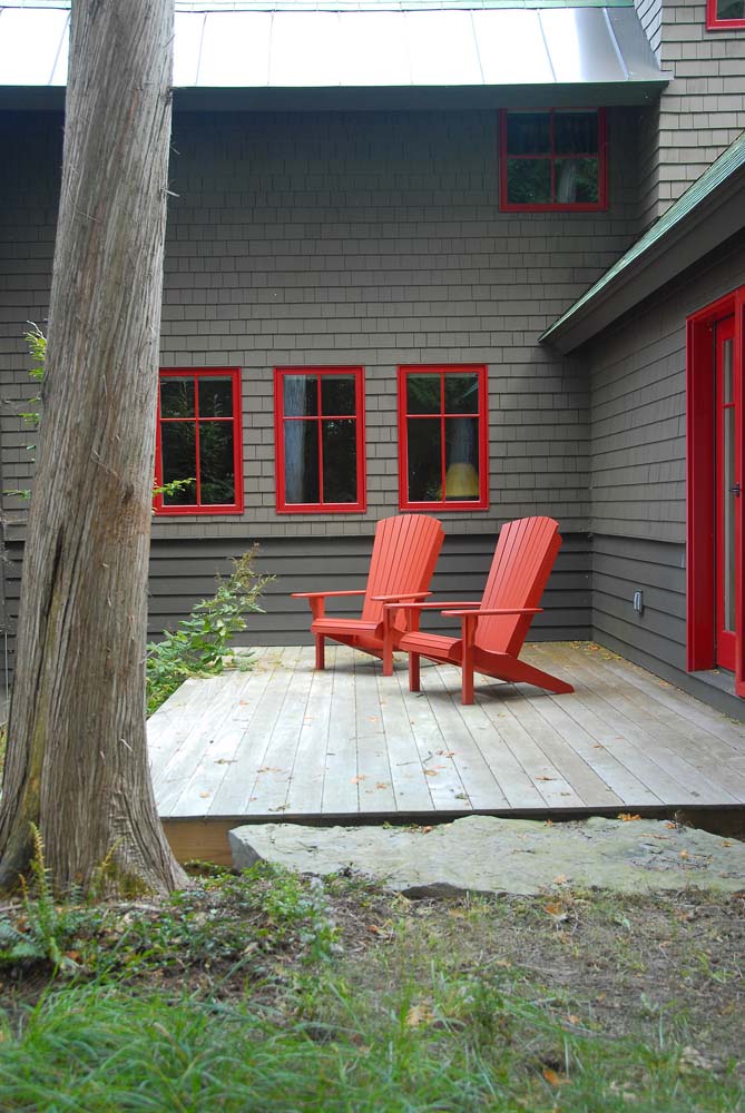 Duas cadeiras vermelhas de madeira para observar a paisagem e relaxar combinando com as janelas dessa casa cinza escura.