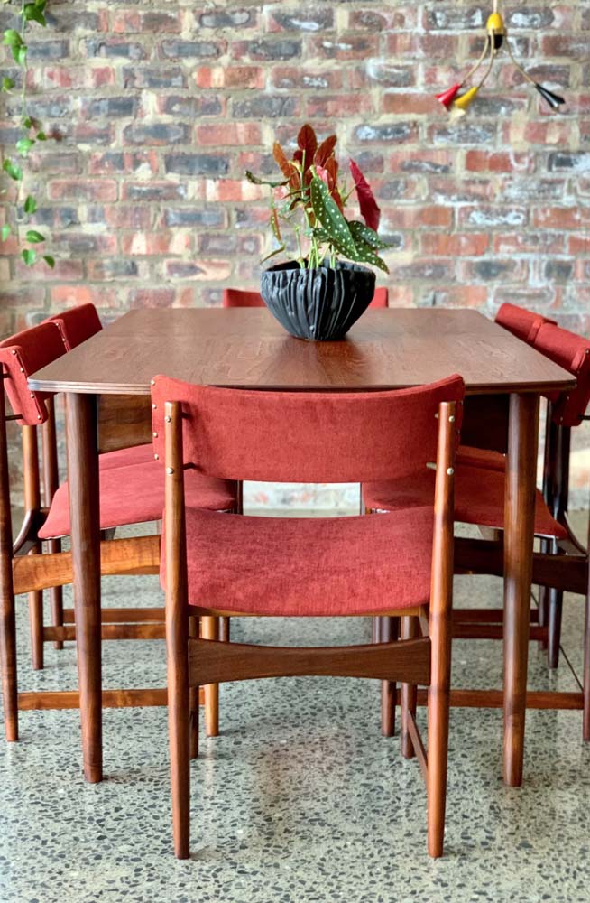 A composição de mesa e cadeiras de madeira com assento e encosto de tecidos vermelhos é sempre um acerto.