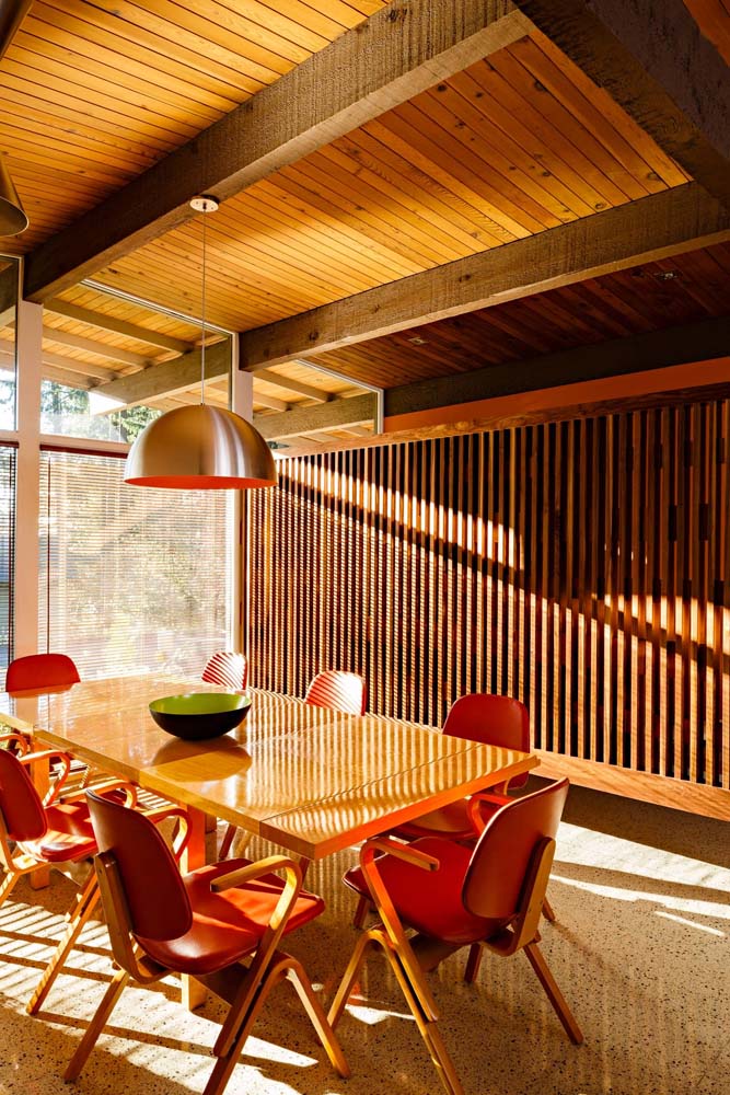Um toque retrô na decoração dessa sala de jantar que aposta na combinação de madeira e vermelho nas suas cadeiras.