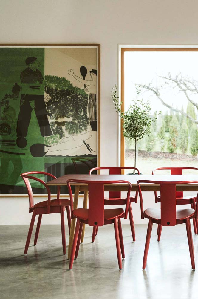Esta sala de jantar moderna e elegante apostou em cadeiras vermelhas na mesa de madeira - contrastando com o verde do poster na parede.