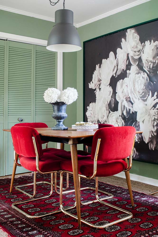 Sala de estar com cadeiras vermelhas estofadas, tapete na mesma cor e flores no vaso e na tela que adornam a decoração. 