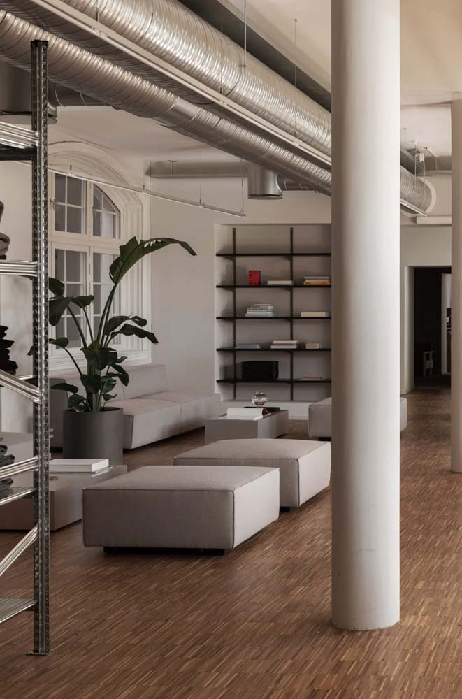 Sofá para escritório moderno, puffs quadrados combinando, estante e vaso grande: espaço simples e elegante para descansar ou recepcionar os cliente.