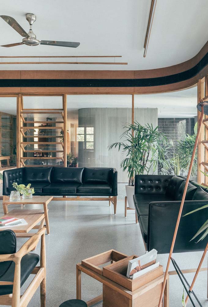 Três sofás de couro preto com pés palito de madeira compõem o ambiente desta recepção de escritório num estilo retrô e elegante.