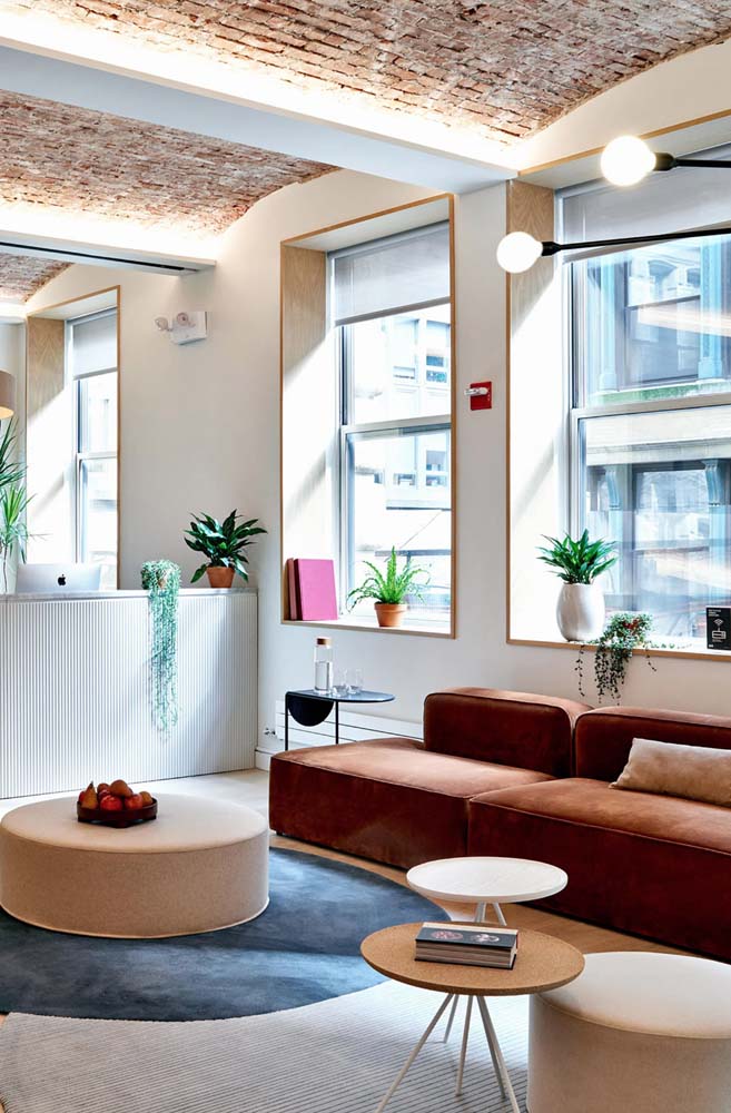 Destaque para o sofá para escritório em tom de terracota nesta recepção moderna e cheia de plantinhas.