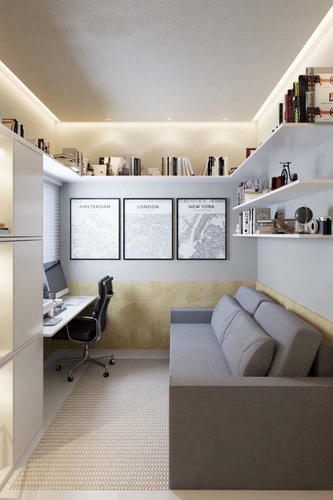 As prateleiras altas garantem armazenamento e liberam espaço para acrescentar o sofá cinza na parede oposta à escrivaninha neste projeto.